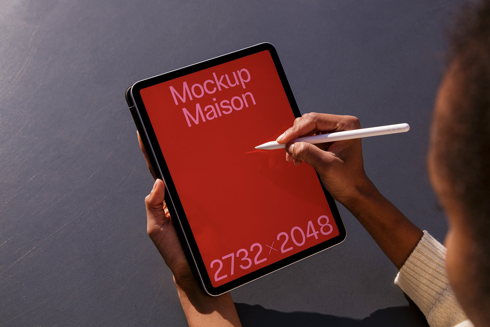 PSD mockup of a tablet with a red screen displaying "Mockup Maison" and "2732 x 2048," held by a person using a stylus.