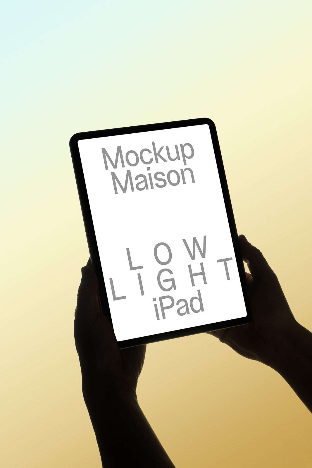PSD mockup of an iPad held in hands with the screen displaying the text "Mockup Maison LOW LIGHT iPad" against a soft gradient background.
