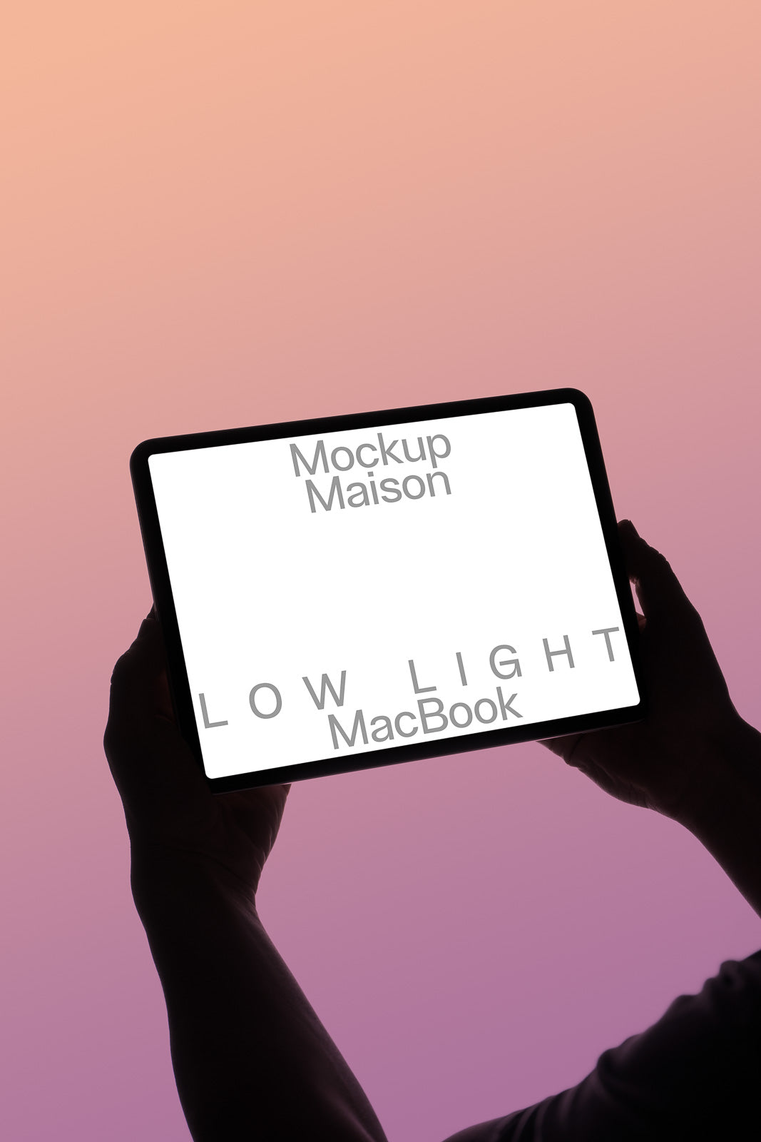 PSD mockup of a person holding a backlit MacBook screen displaying the words "Mockup Maison" and "LOW LIGHT" against a gradient pink-orange background.