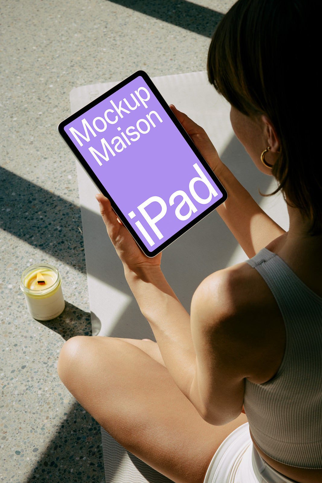 PSD mockup of a person holding an iPad with a purple screen displaying text in a sunlit setting. A lit candle sits nearby.