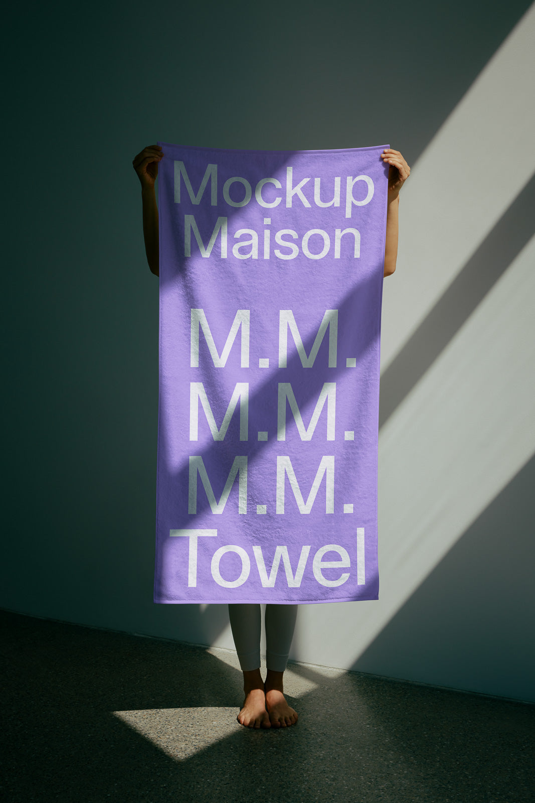 PSD mockup of a person holding a purple towel against a sunlit wall, with the text "Mockup Maison M.M. Towel" in white.