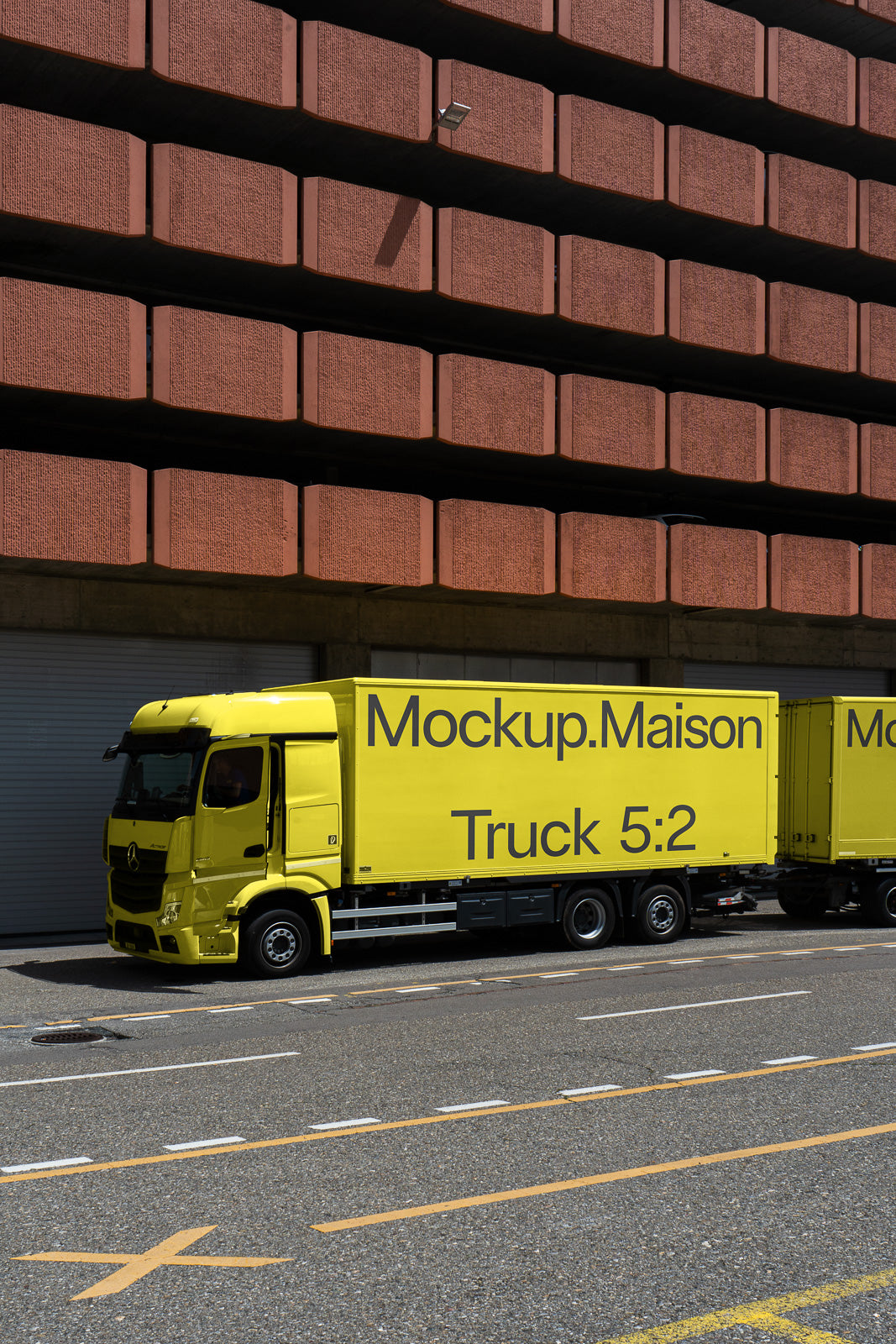PSD mockup of a bright yellow truck with "Mockup.Maison Truck 5:2" text parked beside a red urban building, showcasing its design and branding.