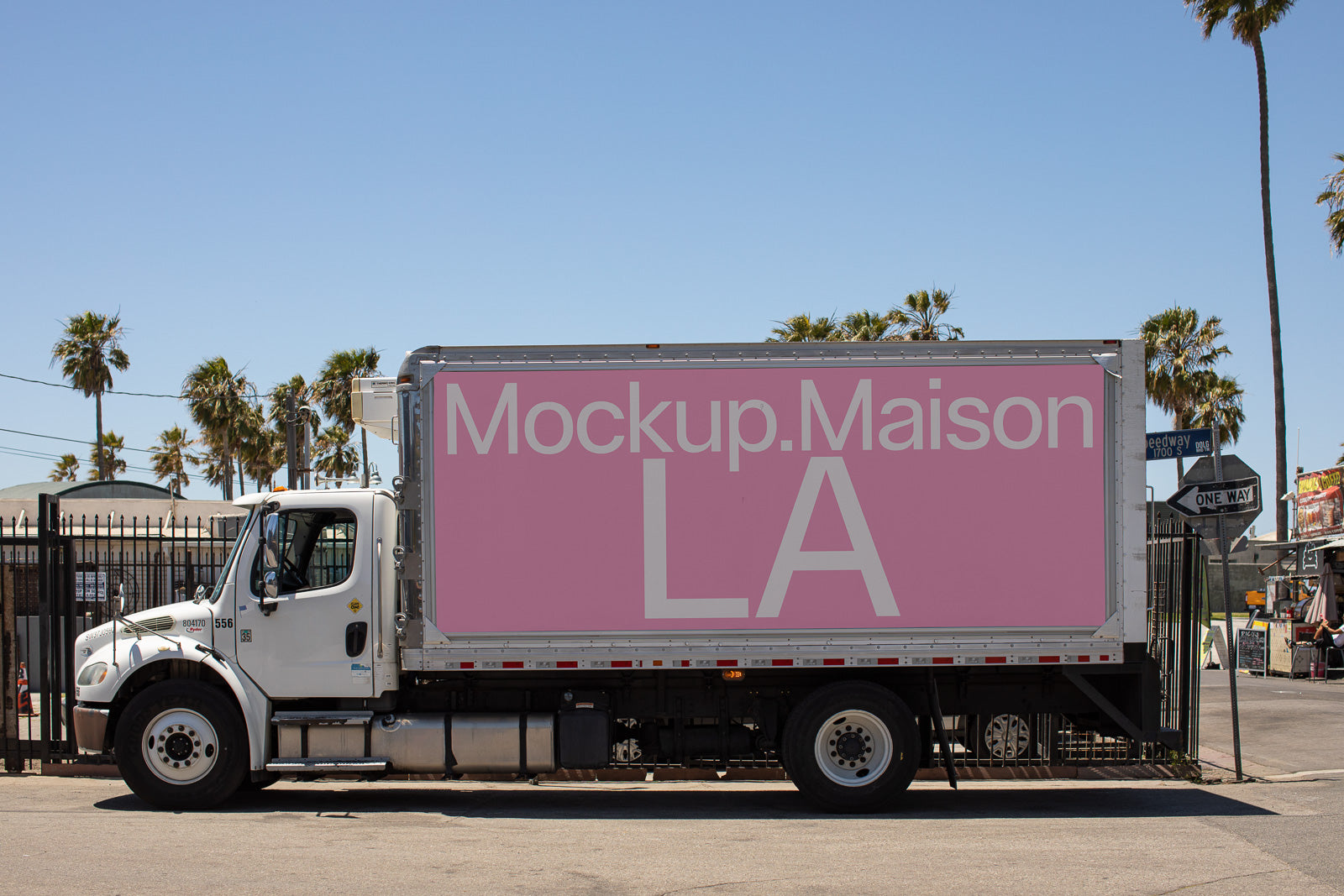 PSD mockup of a large white truck featuring a pink advertising panel with "Mockup.Maison LA" in bold white text, set against a street backdrop.