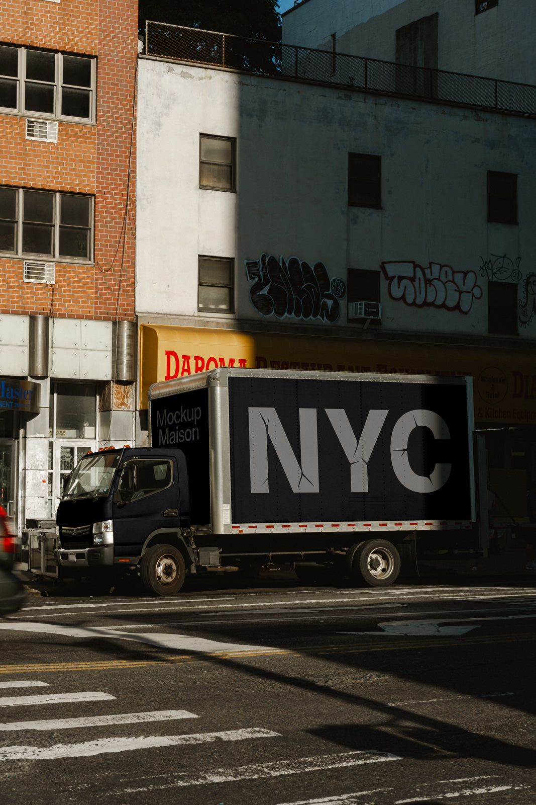 PSD mockup of a delivery truck with "NYC" in bold letters on its side, parked on a city street with graffiti-covered building.