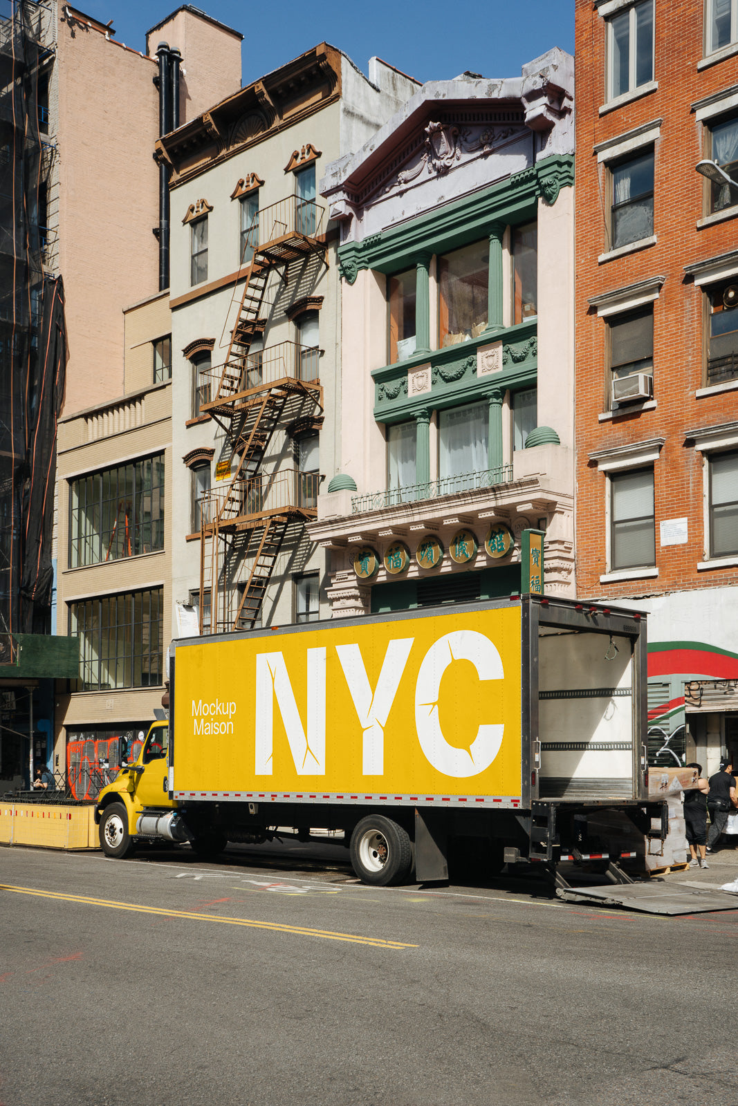 PSD mockup of a yellow delivery truck labeled "NYC" parked on a street in front of historic buildings with fire escapes and ornate facades.