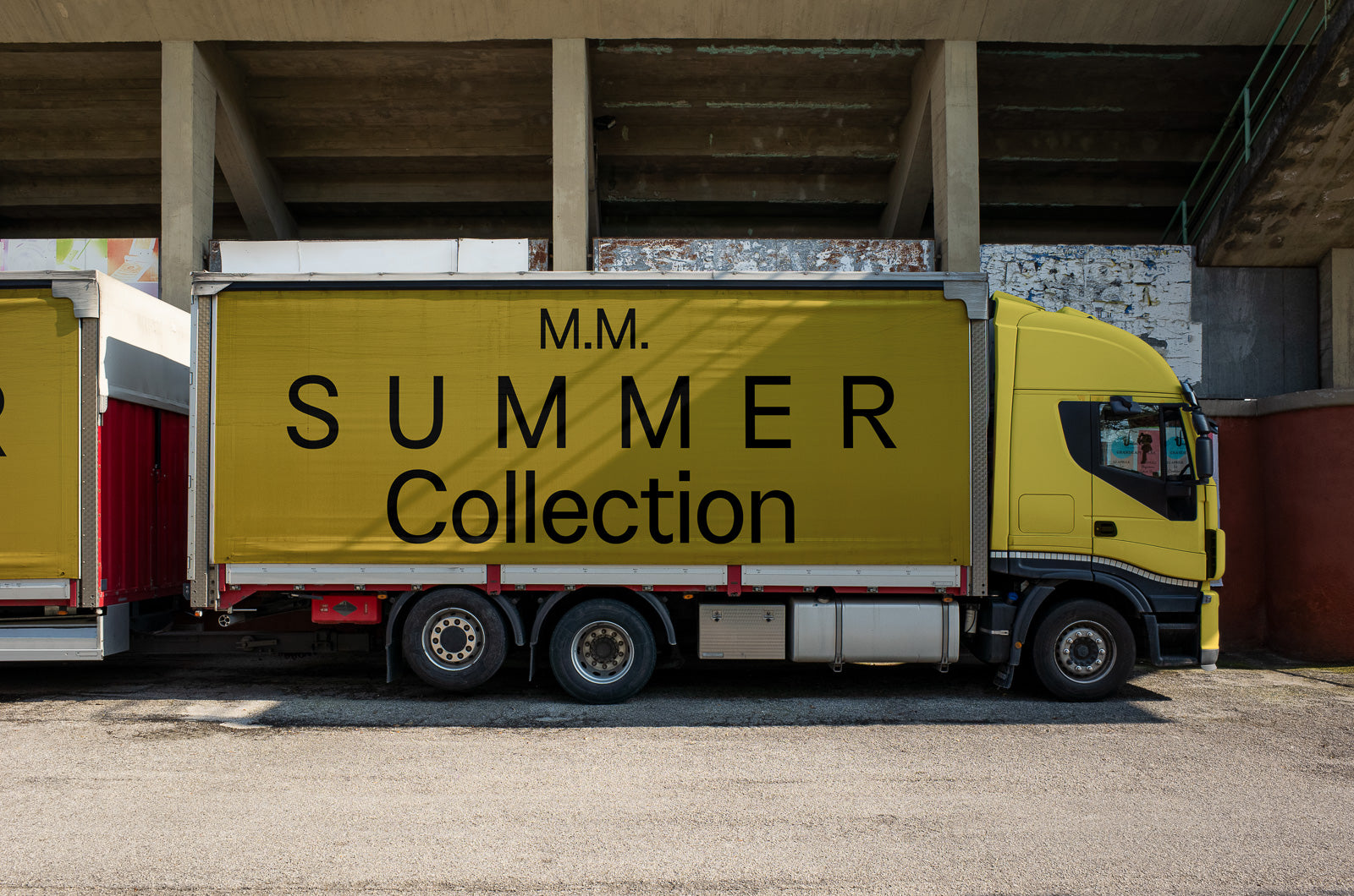 PSD mockup of a yellow delivery truck parked under a concrete structure with bold black text on the side reading "M.M. SUMMER Collection."