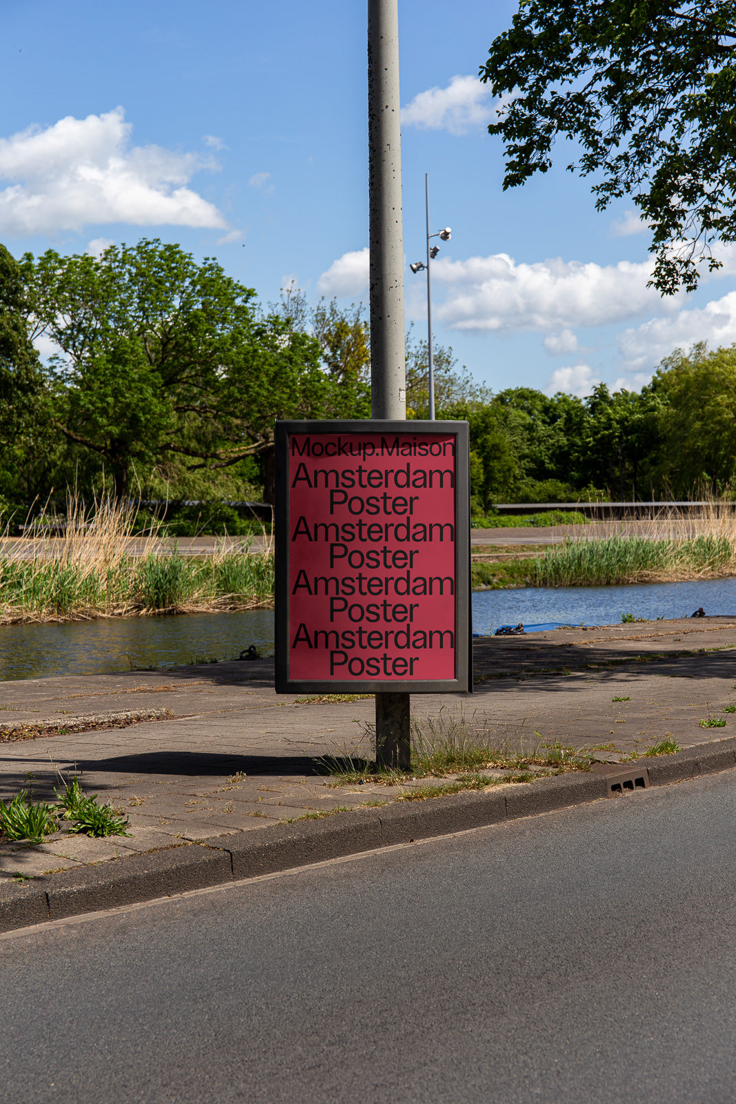 PSD mockup of a roadside poster on a metal pole with a red background, featuring repeated text "Amsterdam Poster," set against a park landscape with trees and a pond.
