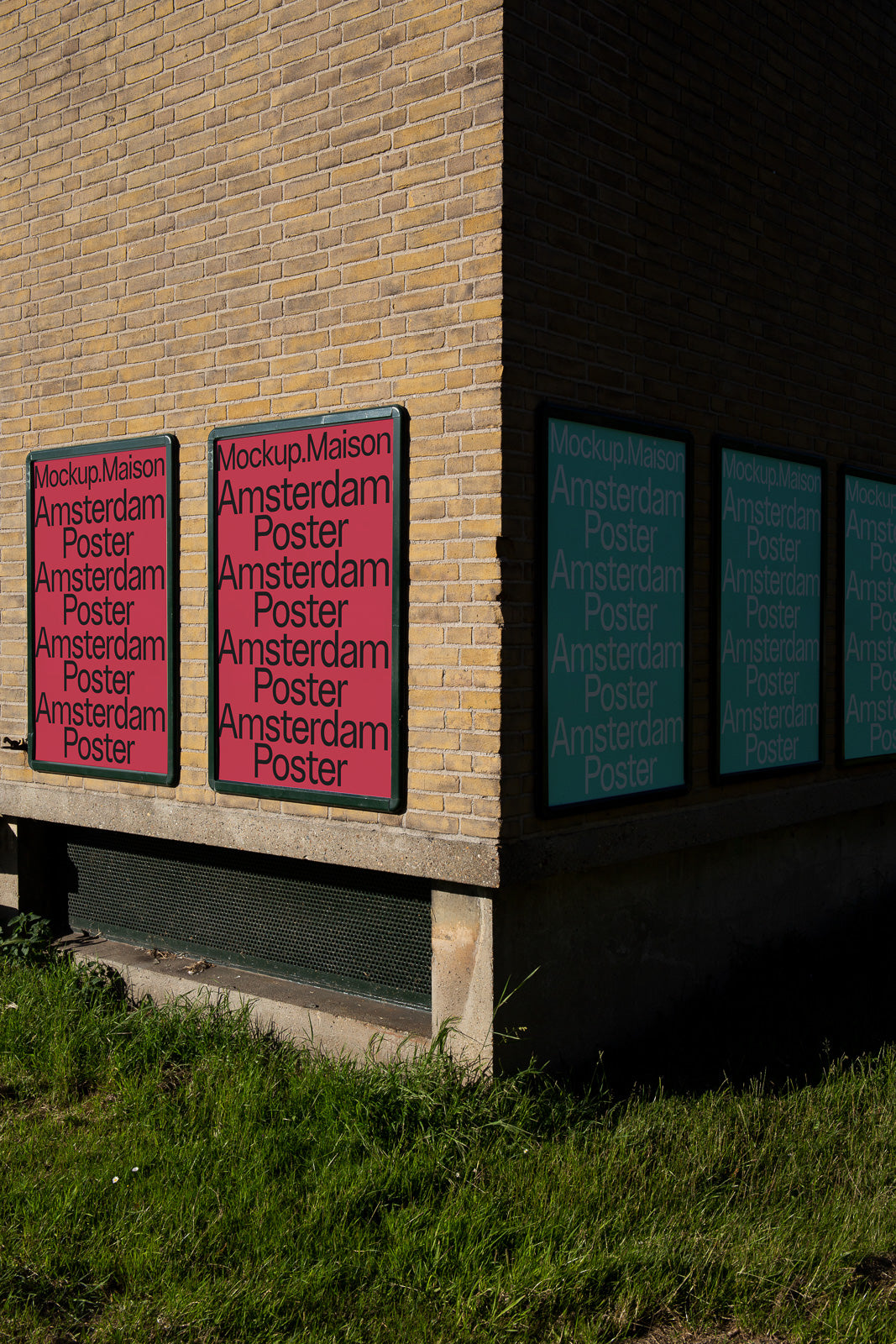 PSD mockup of posters on a brick wall corner, displaying "Amsterdam Poster" in red and green tones in outdoor sunlight.