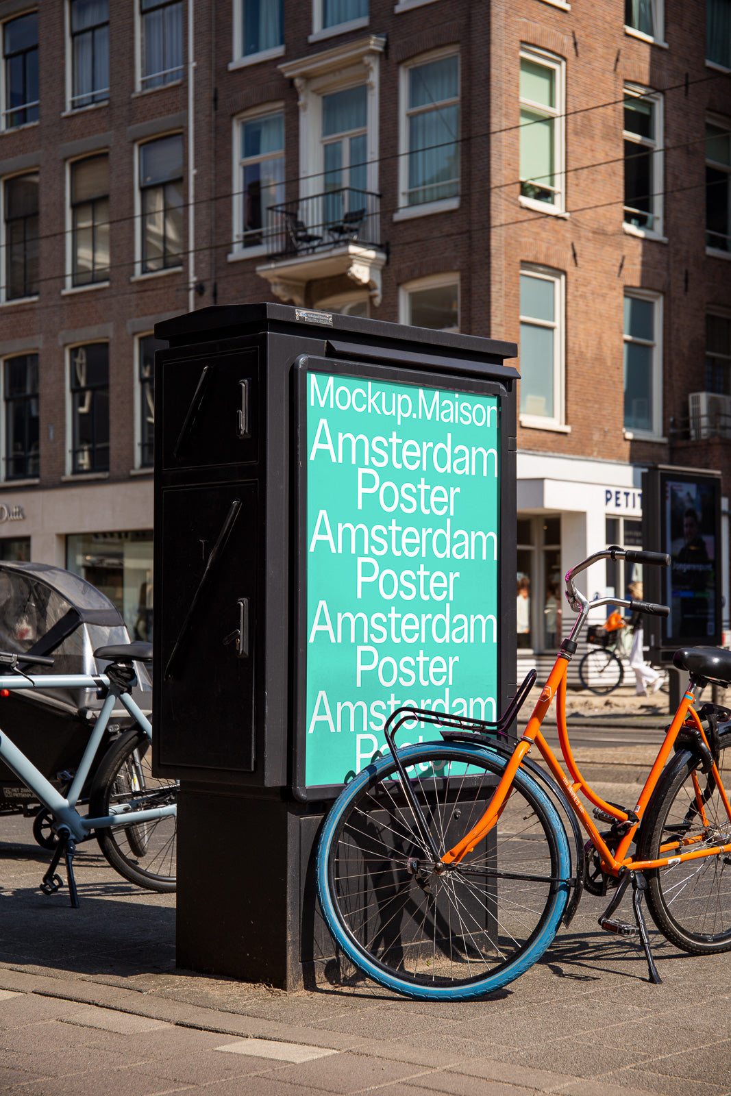 PSD mockup of an urban poster stand featuring the text "Amsterdam Poster" in a city street setting with a bicycle leaning against it.