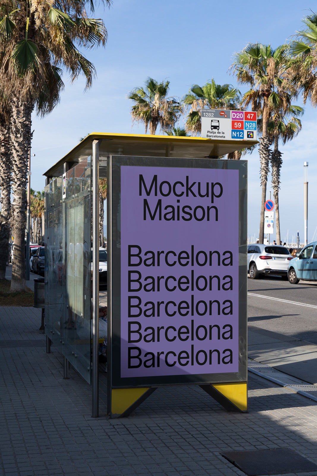 PSD mockup of a bus stop with a large purple poster displaying the text "Mockup Maison Barcelona" repeatedly, set on a sunny street lined with palm trees.