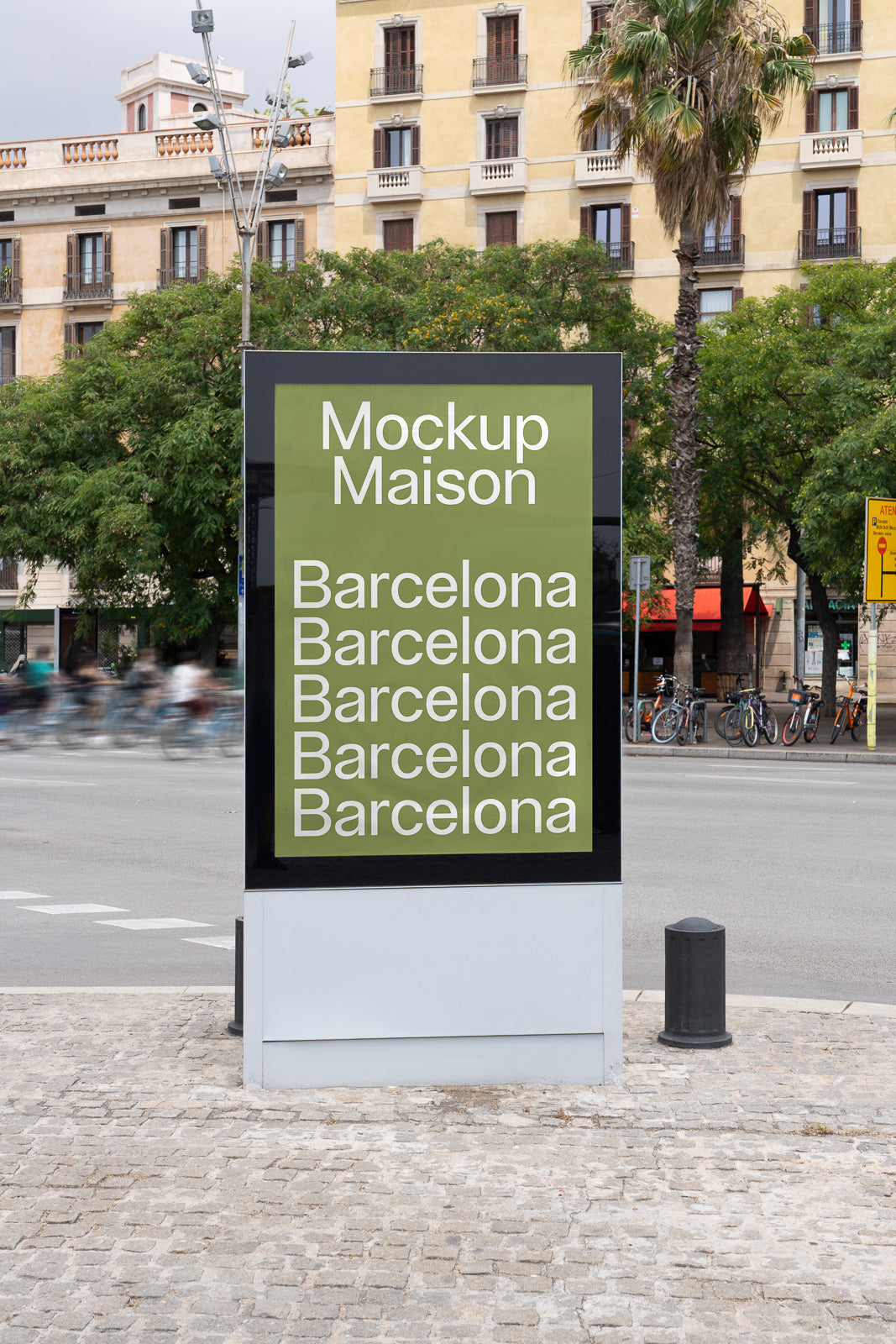PSD mockup of an outdoor advertising stand on a city sidewalk with the words "Mockup Maison" and "Barcelona" repeated, set against an urban background with trees and a building.
