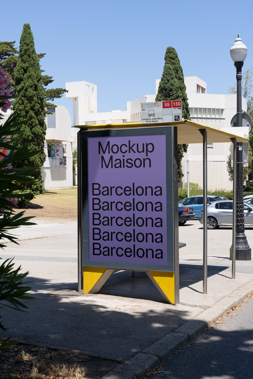 PSD mockup of a bus stop billboard displaying "Mockup Maison" and "Barcelona" multiple times, set against an outdoor urban background with trees and buildings.