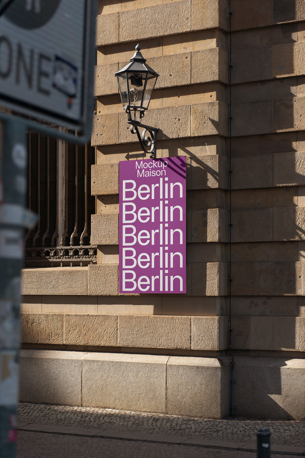 PSD mockup of a purple sign with the word "Berlin" repeated in white, attached to a stone building wall under a vintage lantern.