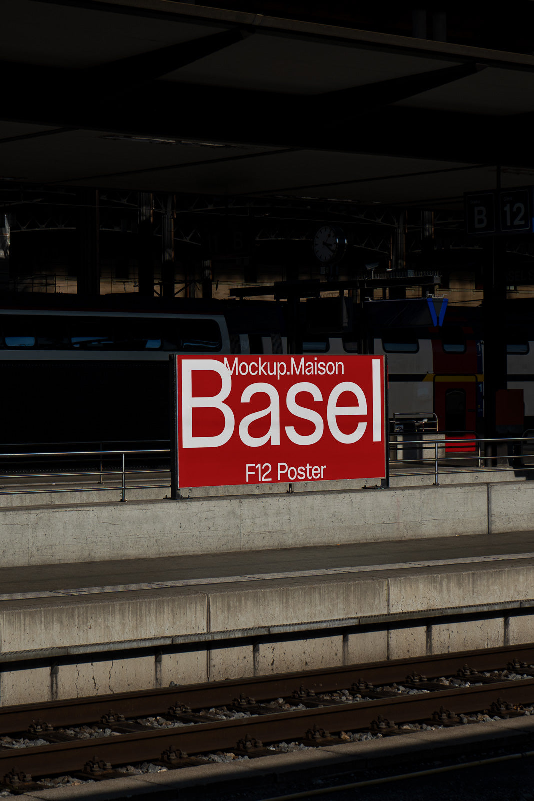 PSD mockup of a red and white poster displayed at a train station platform, with tracks in the foreground and a train partially visible in the background.