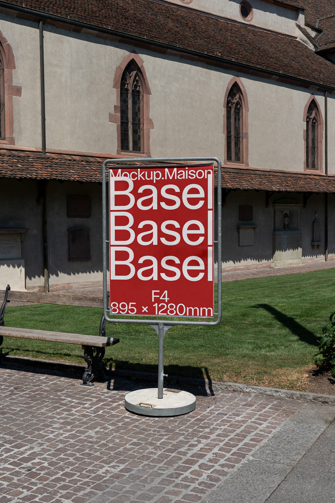 PSD mockup of a red signage stand with white text including measurements, positioned on a cobblestone path beside a historic building.