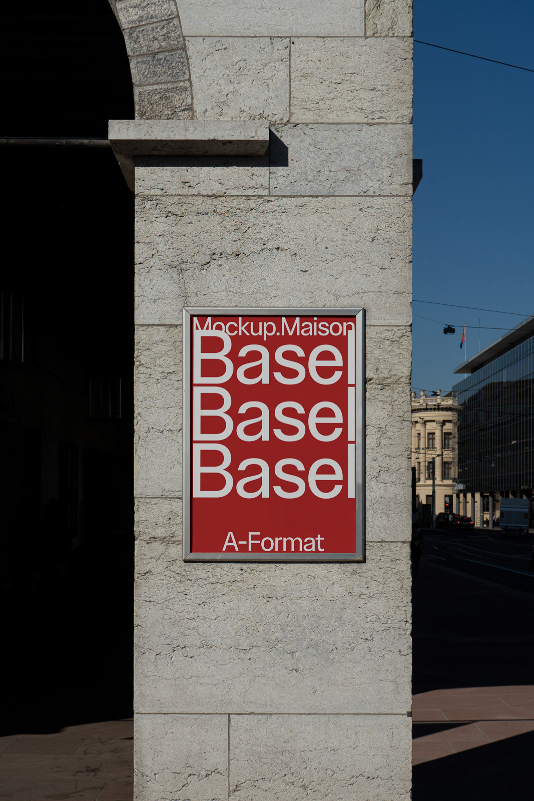 PSD mockup of a poster on a stone wall displaying the word "Basel" in bold white text on a red background with architectural elements in view.