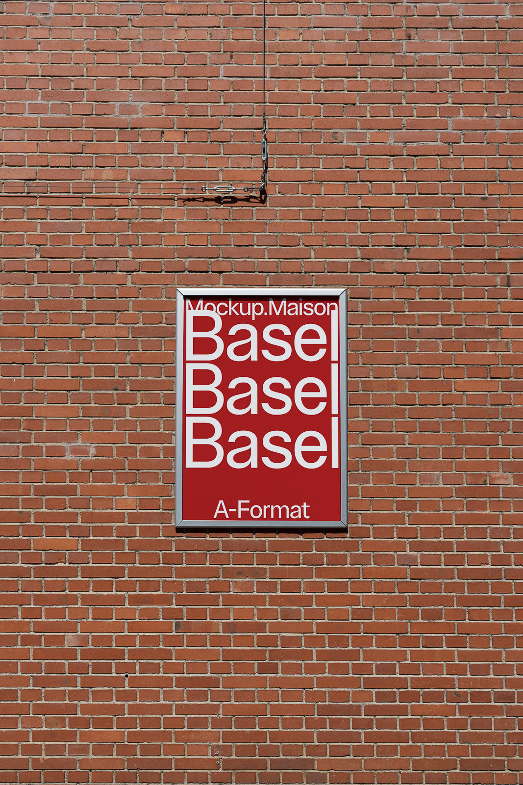 PSD mockup of a red and white vertical poster on a brick wall, displaying the text "Mockup.Maison Basel Basel Basel A-Format" with a chain hanging above.