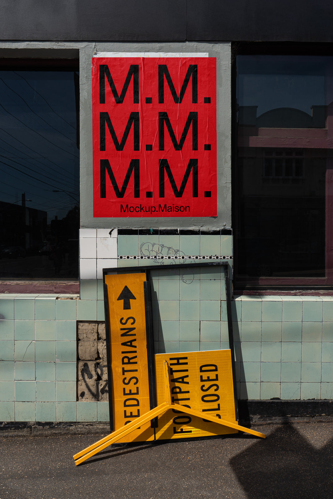 PSD mockup of a red poster with repeated black "M.M." letters on a gray wall, accompanied by yellow traffic signs leaning below.