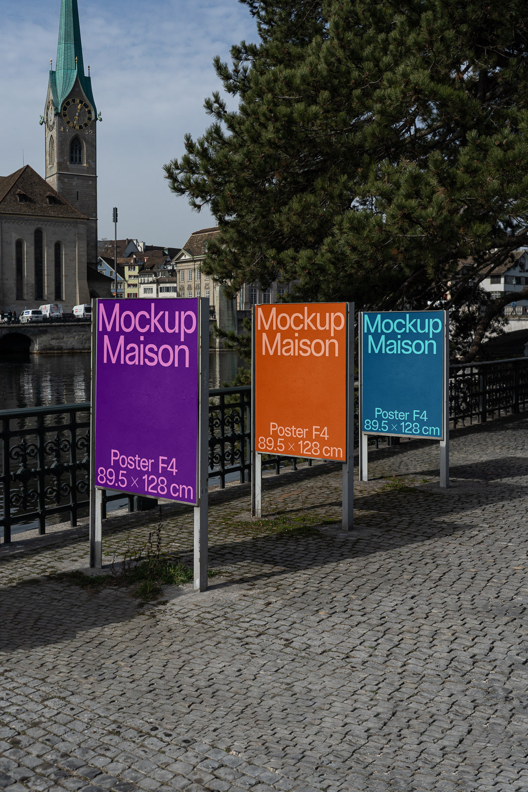 PSD mockup of three colorful F4 poster stands along a cobblestone path, with a scenic view of a historic building and church tower in the background.