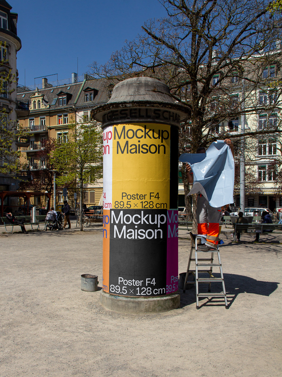 PSD mockup of a cylindrical street advertising pillar with multiple colorful poster designs, surrounded by an urban setting with trees and buildings.