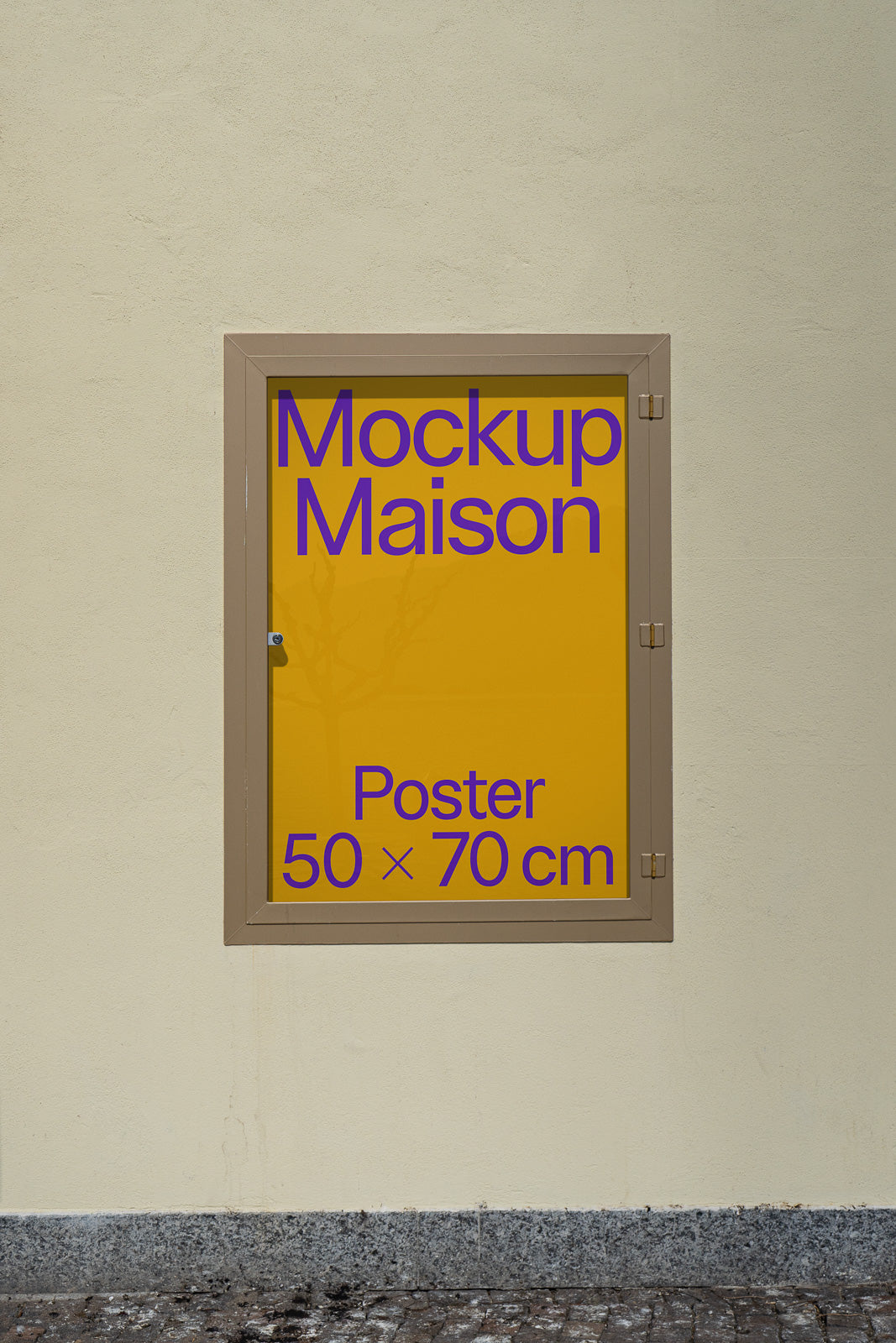 PSD mockup of a framed yellow poster with "Mockup Maison" text, measuring 50x70 cm, placed on a textured wall above a stone pavement.