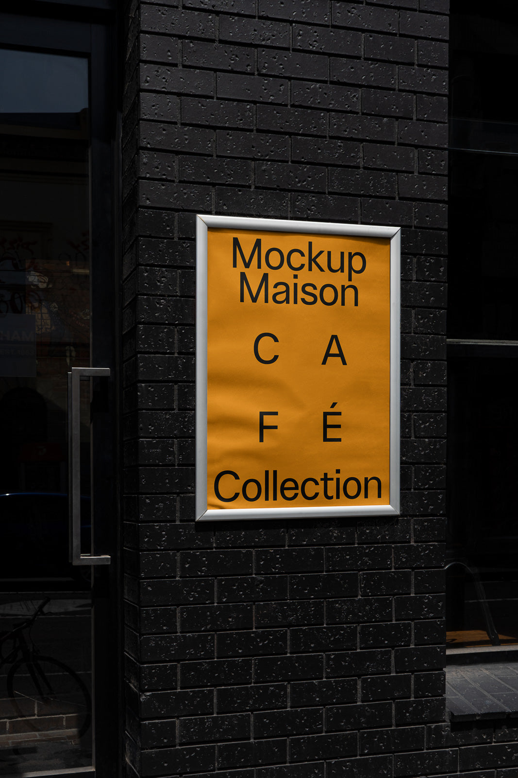 PSD mockup of an orange poster with black text that reads "Mockup Maison Café Collection" displayed on a dark brick wall.