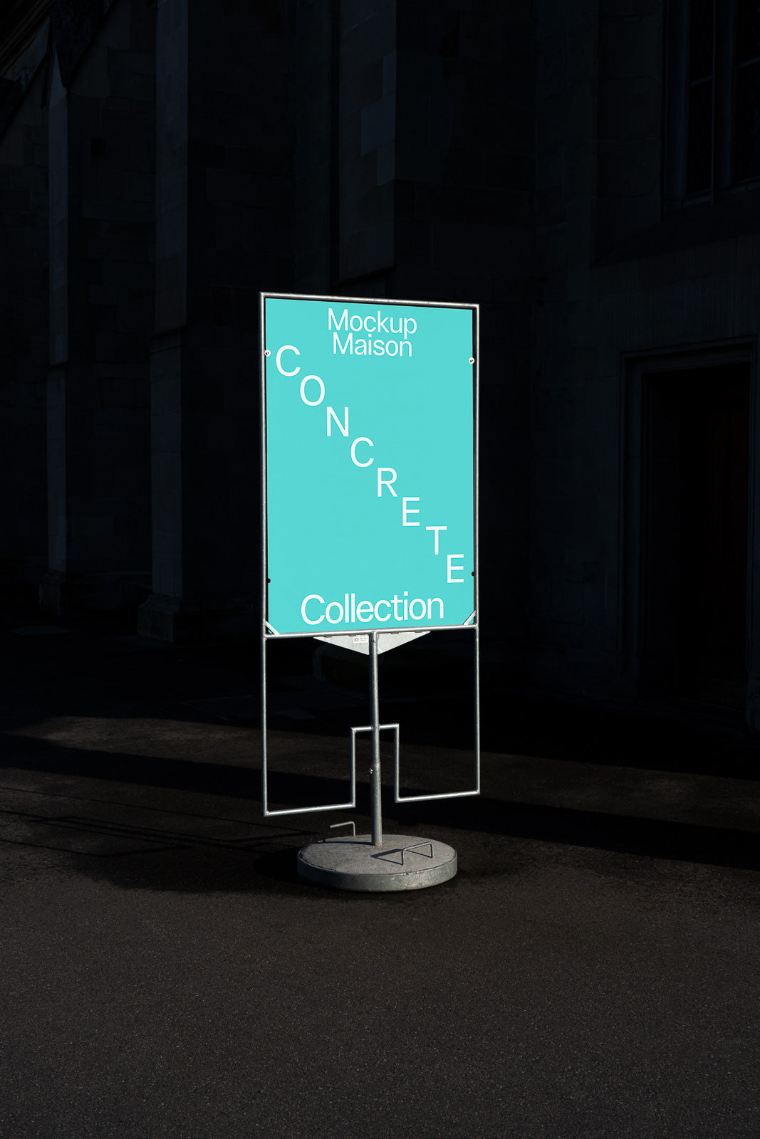 PSD mockup of a freestanding outdoor sign displaying "Mockup Maison Concrete Collection" in white text on a teal background in a dimly lit urban setting.
