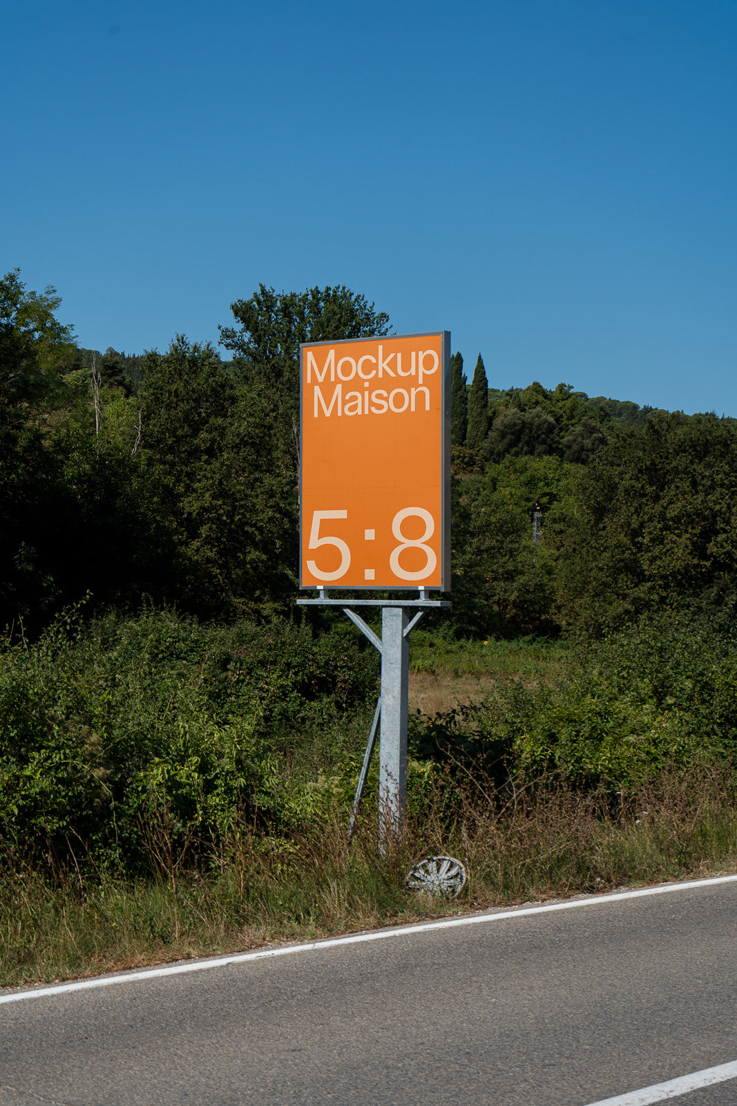PSD mockup of a roadside sign displaying "Mockup Maison 5:8" on an orange background, surrounded by lush greenery and trees.