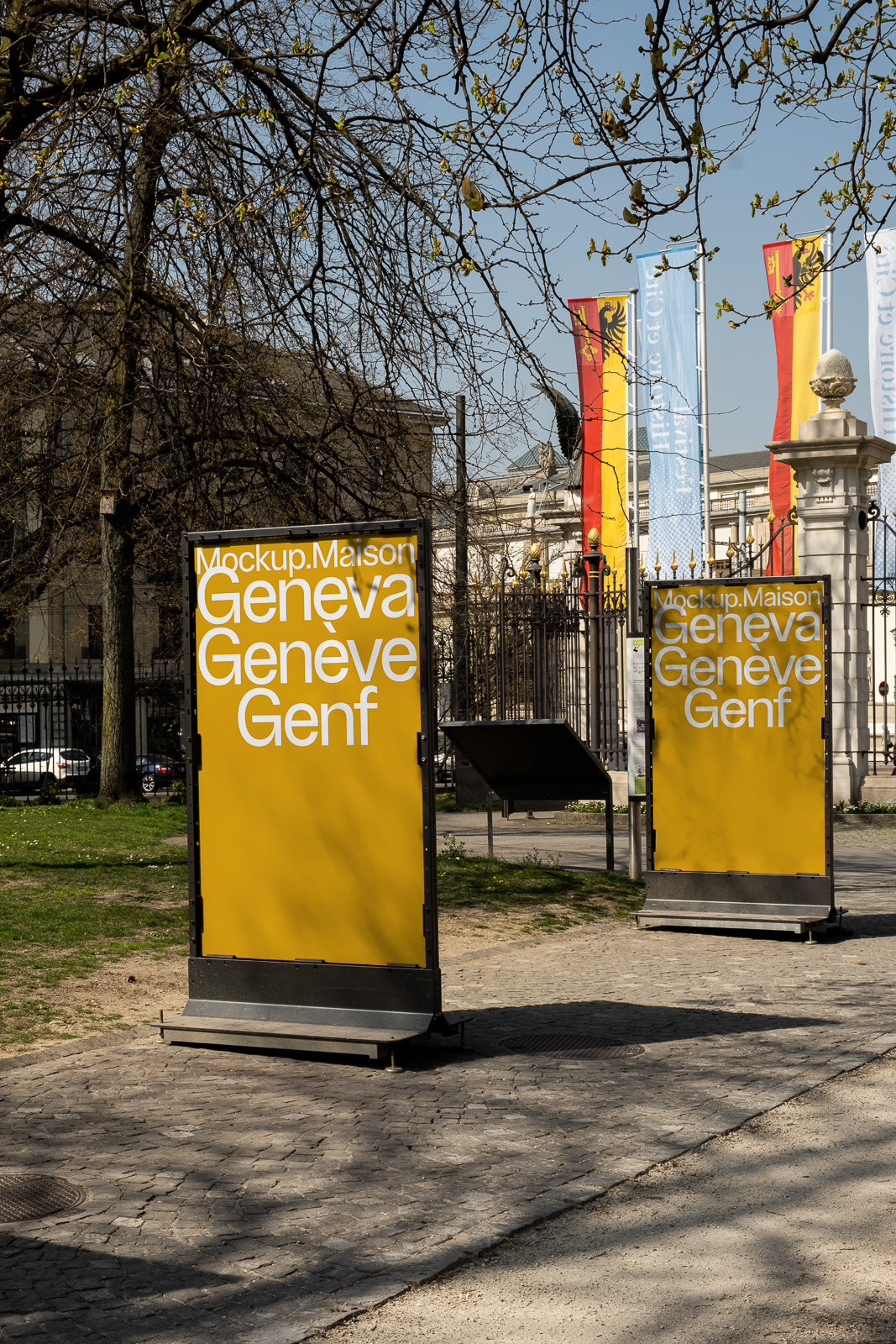 PSD mockup of two yellow billboards in a park setting, displaying the text "Mockup.Maison Geneva Geneve Genf" with trees and flags in the background.