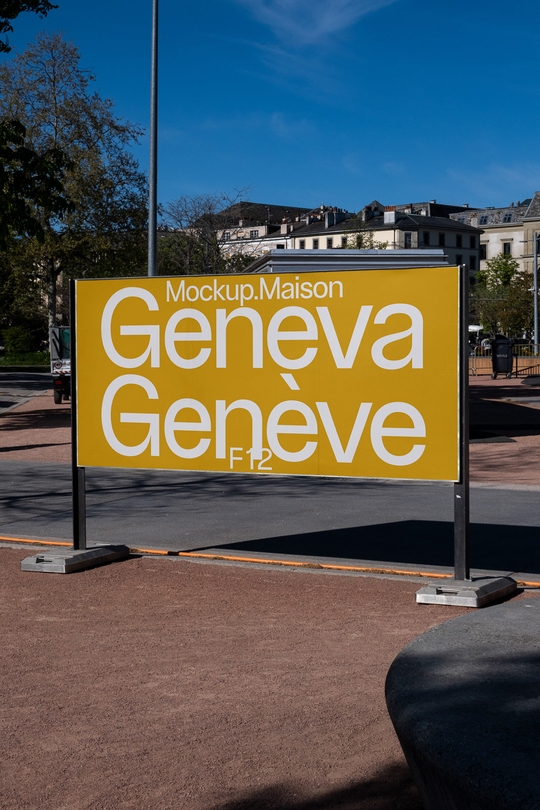 PSD mockup of a large outdoor sign with bold yellow background displaying the text "Mockup.Maison Geneva Genève" against an urban backdrop with blue sky.