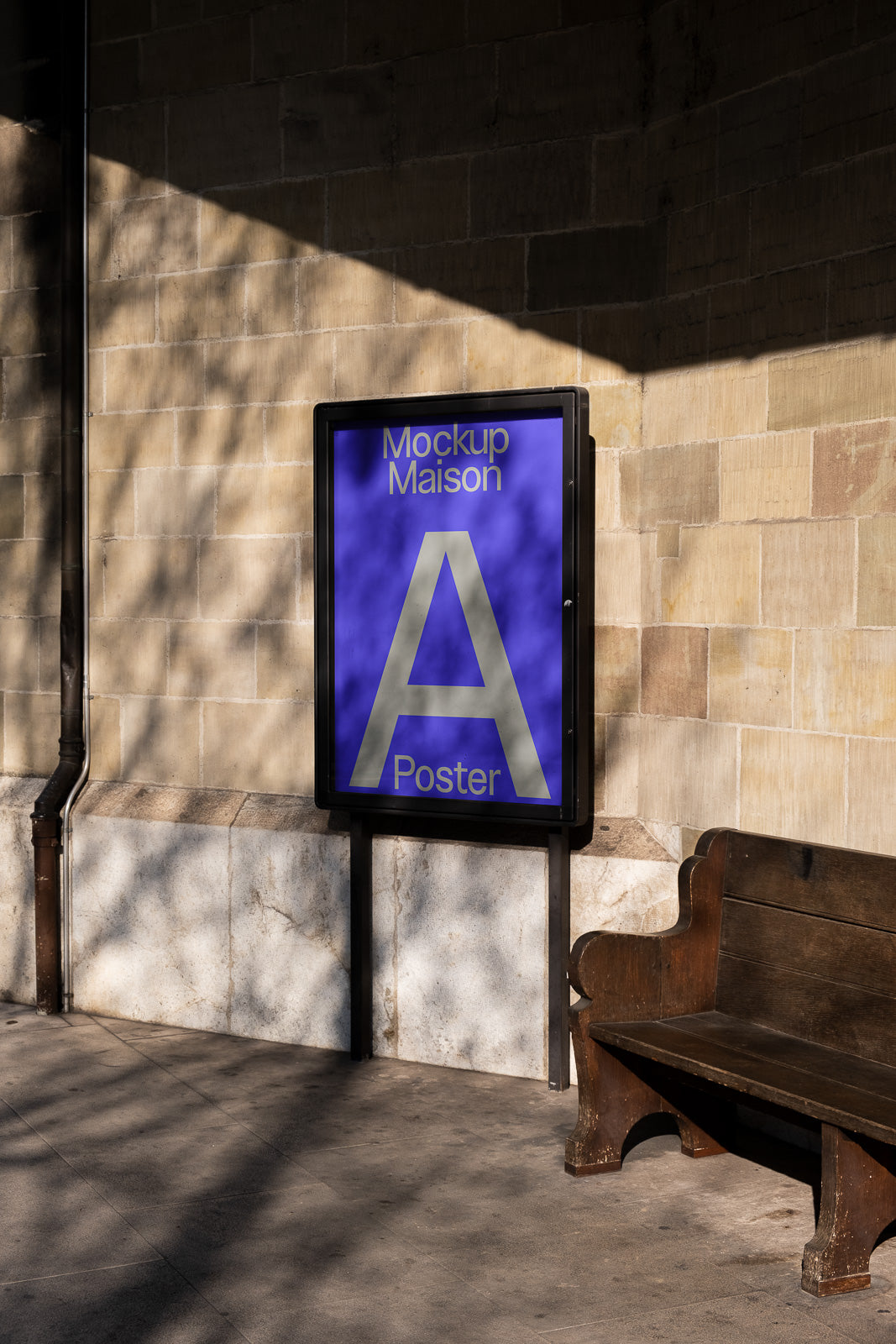 PSD mockup of an outdoor poster display on a wall in a shaded area beside a wooden bench. The poster features the text "Mockup Maison A Poster" in blue.