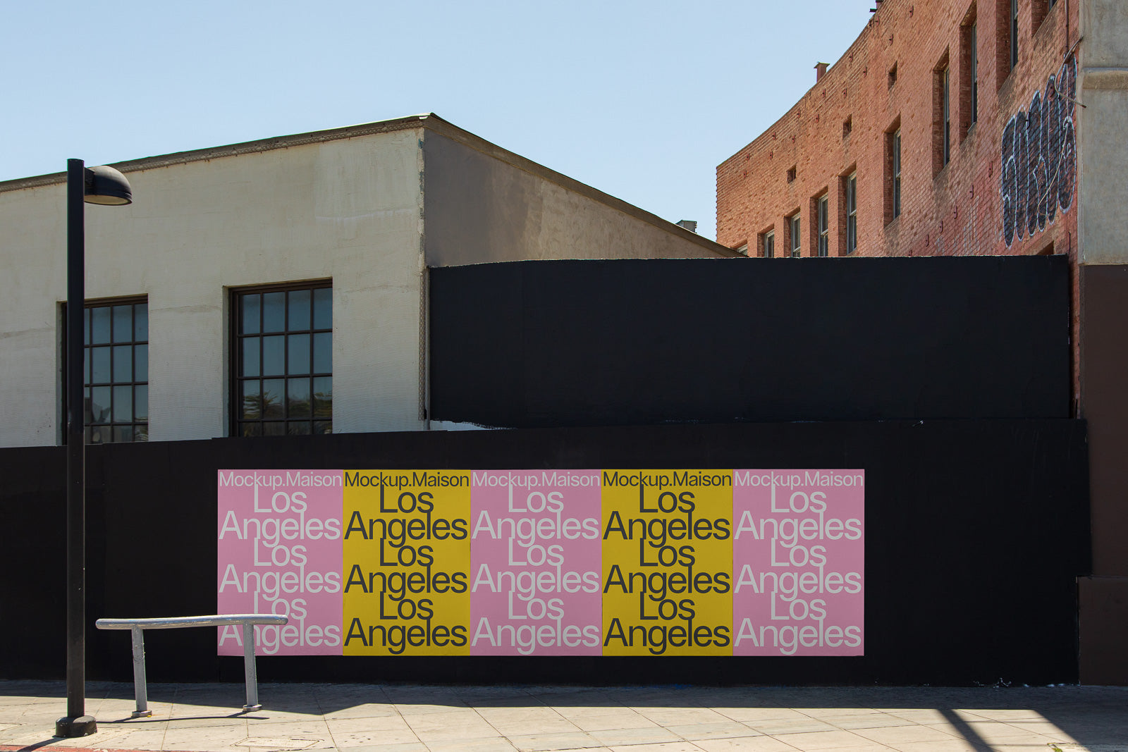 PSD mockup of a series of posters displaying the text "Los Angeles" in pink and yellow on a black wall outside a building with windows.