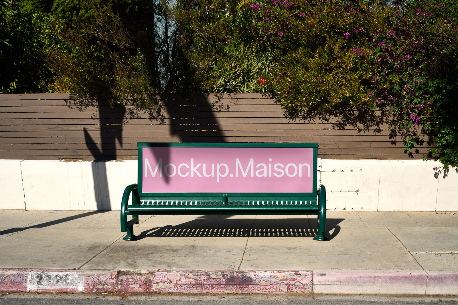 PSD mockup of a green bench with an advertisement board displaying the text "Mockup.Maison" against a background of trees and a wooden fence.