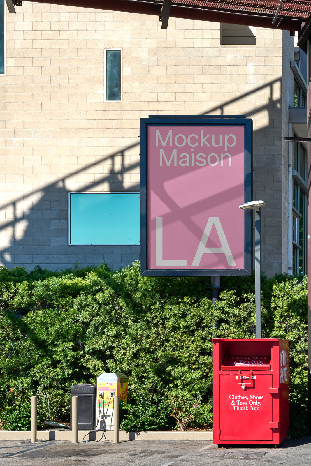 PSD mockup of a large outdoor billboard displaying "Mockup Maison LA" in a pink color scheme, set against a brick wall and framed by greenery.