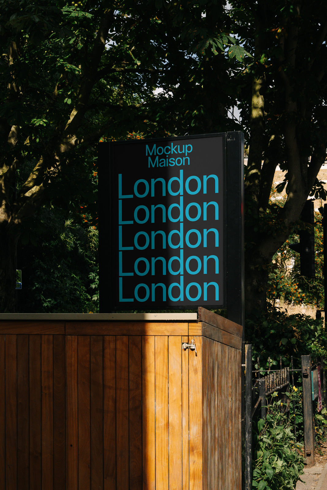 PSD mockup of a vertical outdoor sign featuring repeated blue text “London” beneath “Mockup Maison” against a black background surrounded by greenery.
