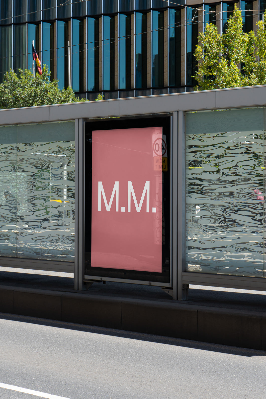 PSD mockup of a pink billboard at an urban bus stop with the letters "M.M." displayed in white.