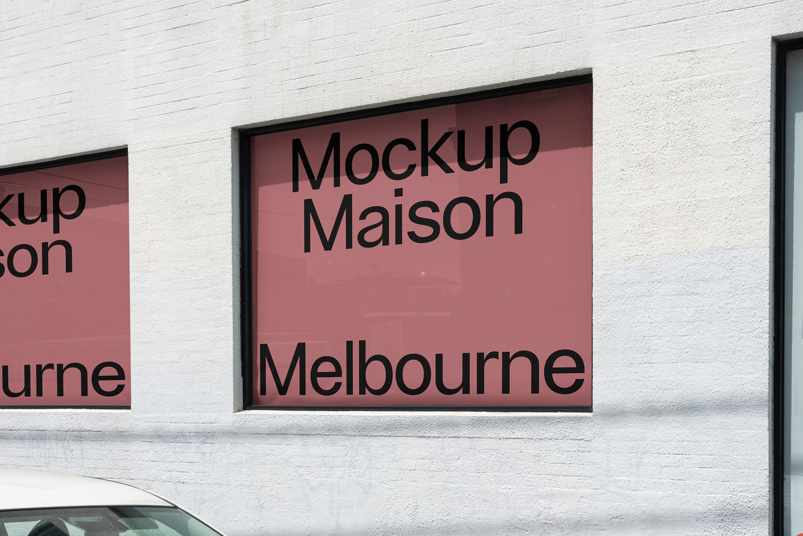 PSD mockup of a storefront window featuring text "Mockup Maison Melbourne" on a pink background, placed on a white brick wall, partially visible car below.