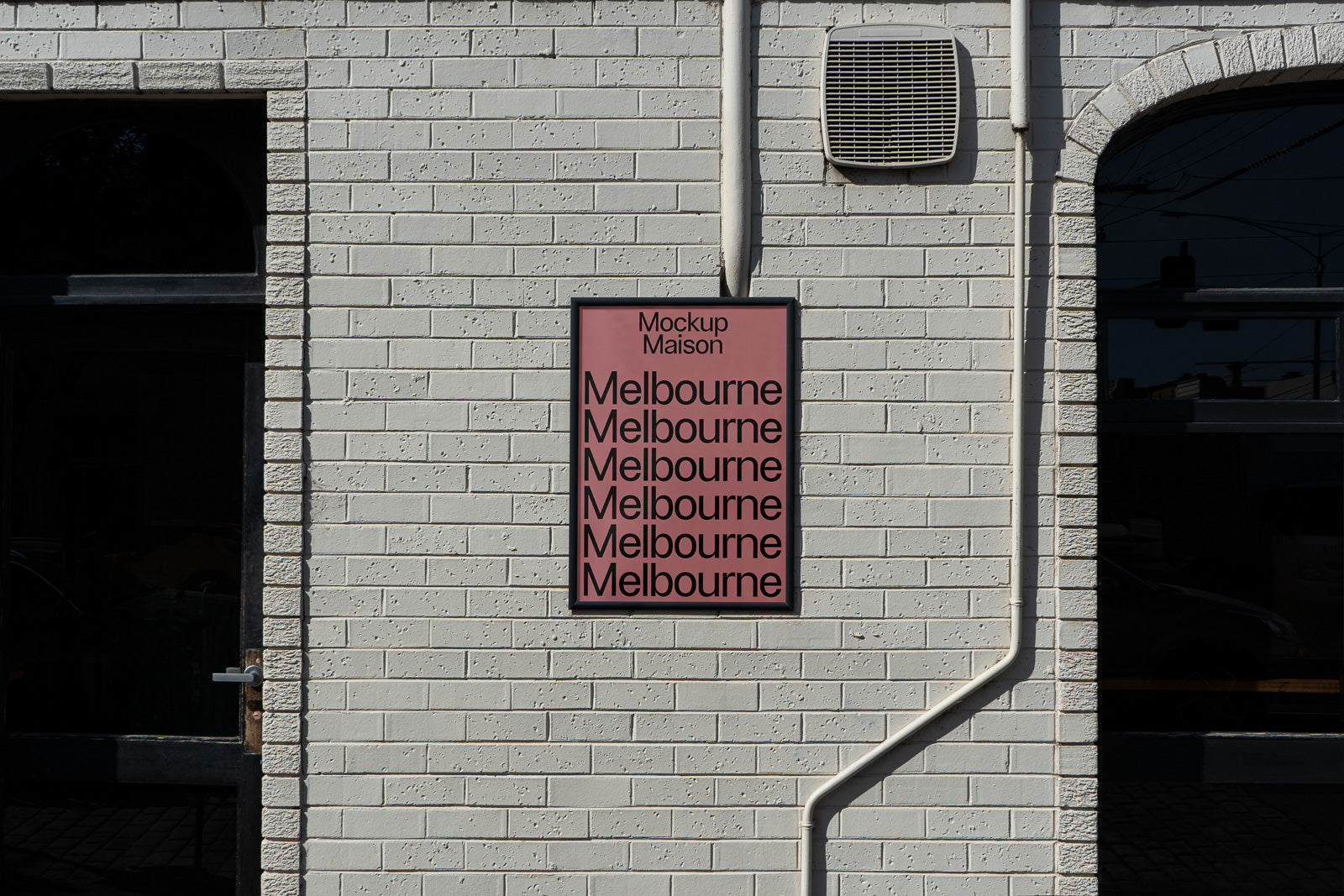 PSD mockup of a wall-mounted poster featuring repeated text "Melbourne" in bold black font on a reddish background, set against a white brick wall.