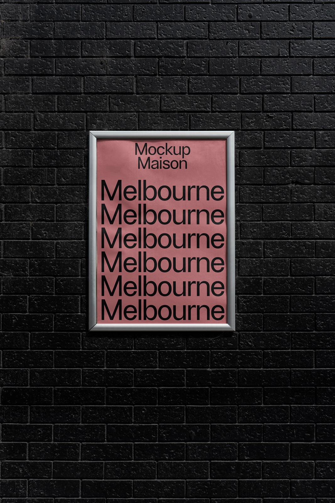 PSD mockup of a silver-framed poster with "Mockup Maison" title and multiple "Melbourne" texts on a pink background against a black brick wall.