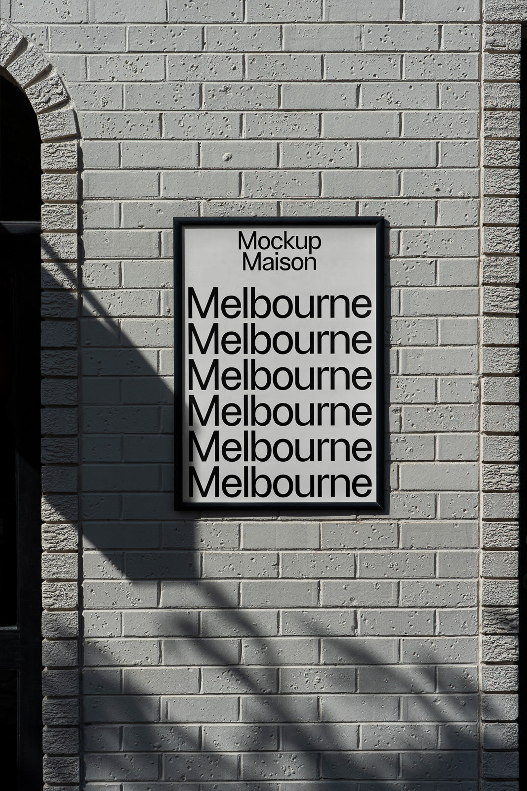 PSD mockup of a framed poster on a textured brick wall displaying the word "Melbourne" repeatedly in bold black text.