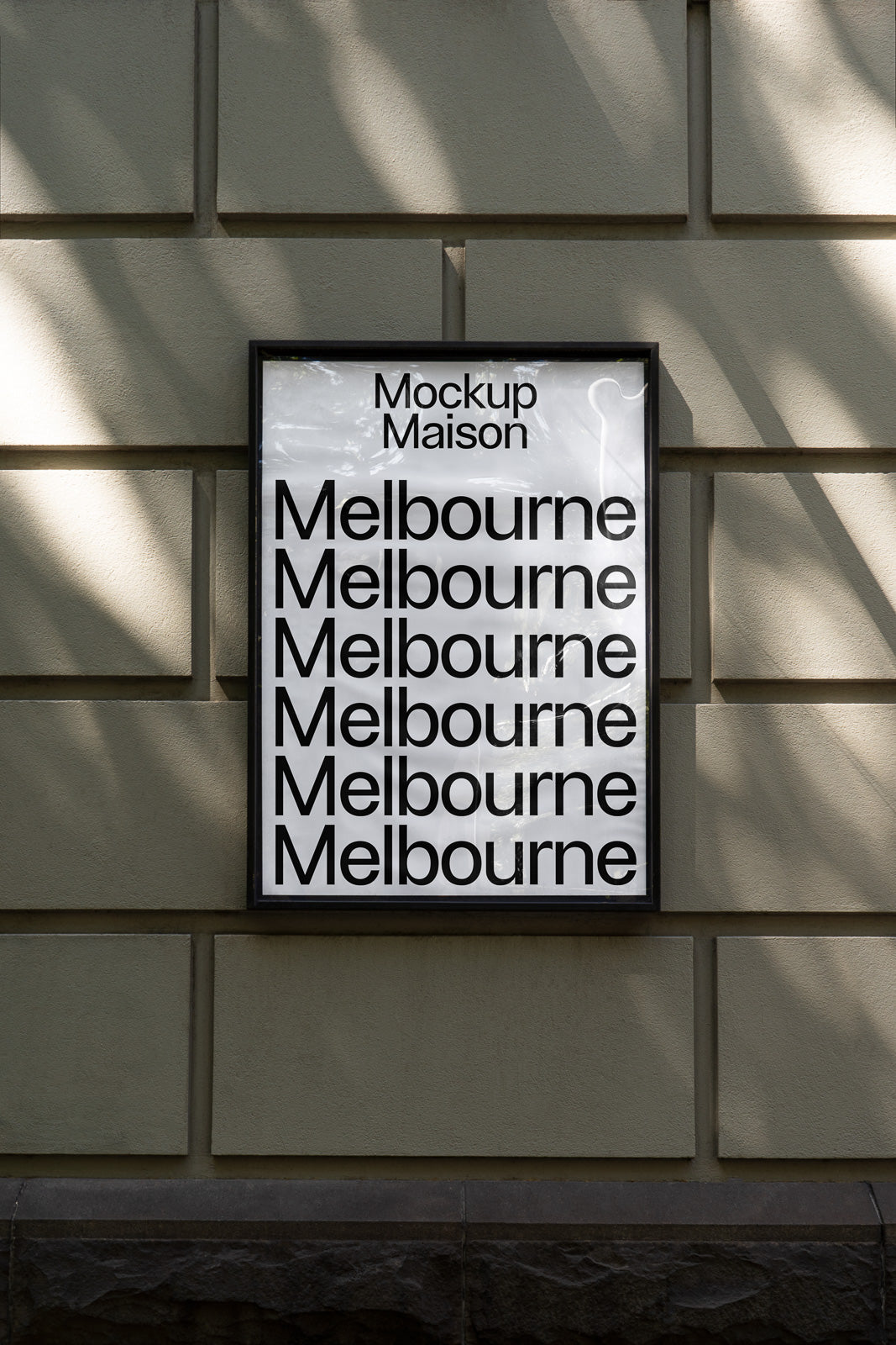 PSD mockup of a framed poster on a textured stone wall, displaying repetitive text "Melbourne" in bold, sans-serif font with shadows.