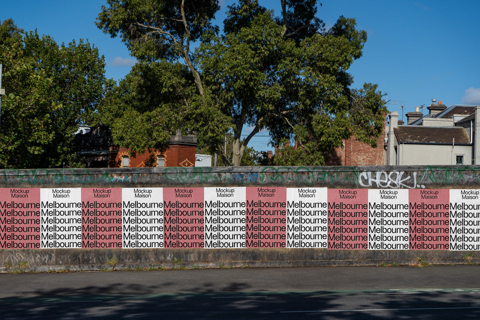 PSD mockup of a real-life wall covered in repetitive "Melbourne" posters under a clear blue sky, with trees and urban buildings in the background.