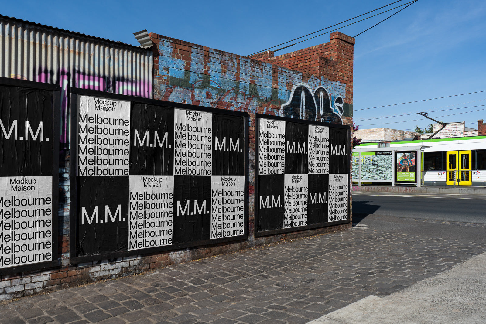 PSD mockup of posters on a brick wall with alternating black and white text "M.M." and "Melbourne," set in an urban street scene with a tram passing by.