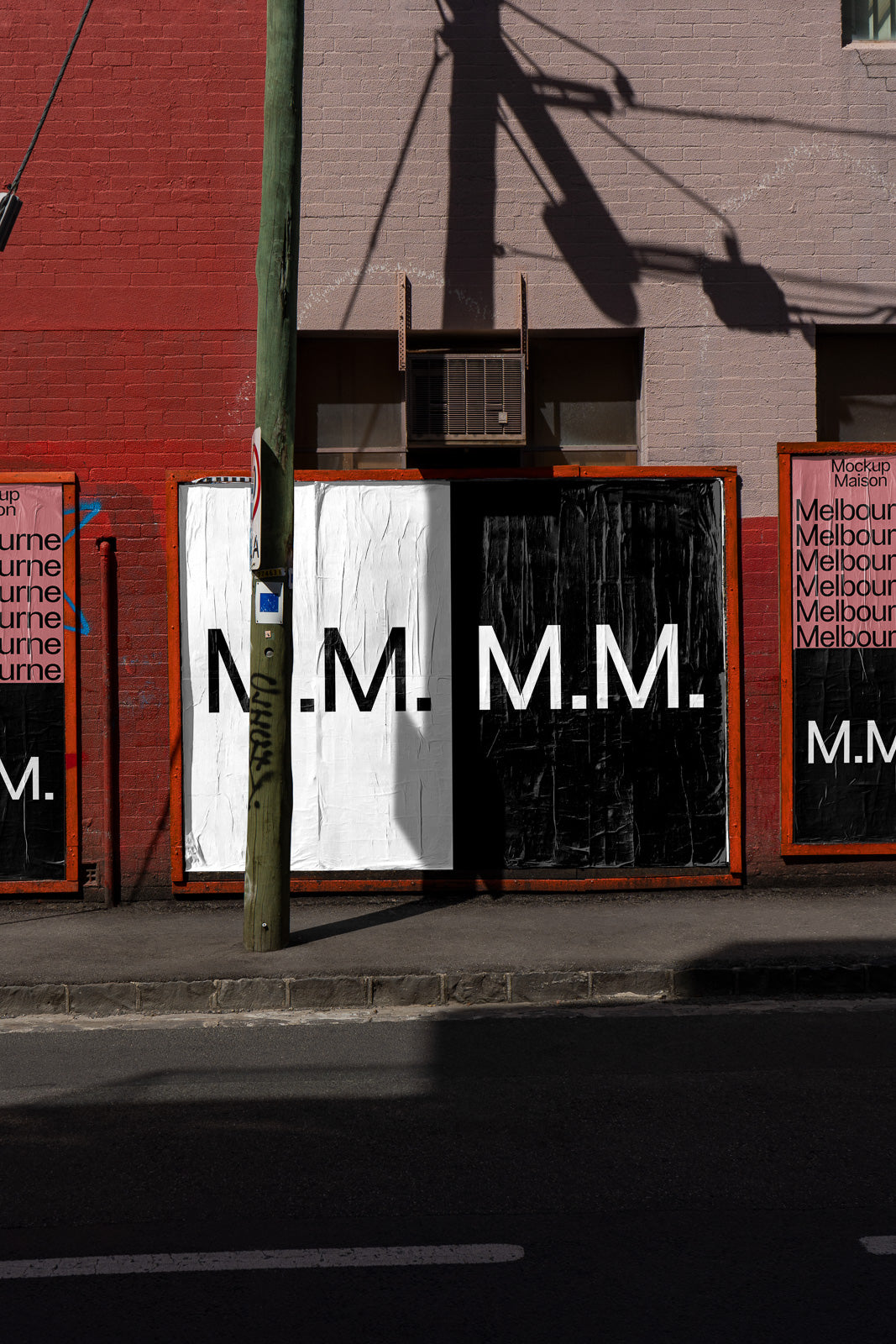 PSD mockup of urban posters with bold "M.M." graphics on a textured wall, featuring red and black color schemes under city street shadows.