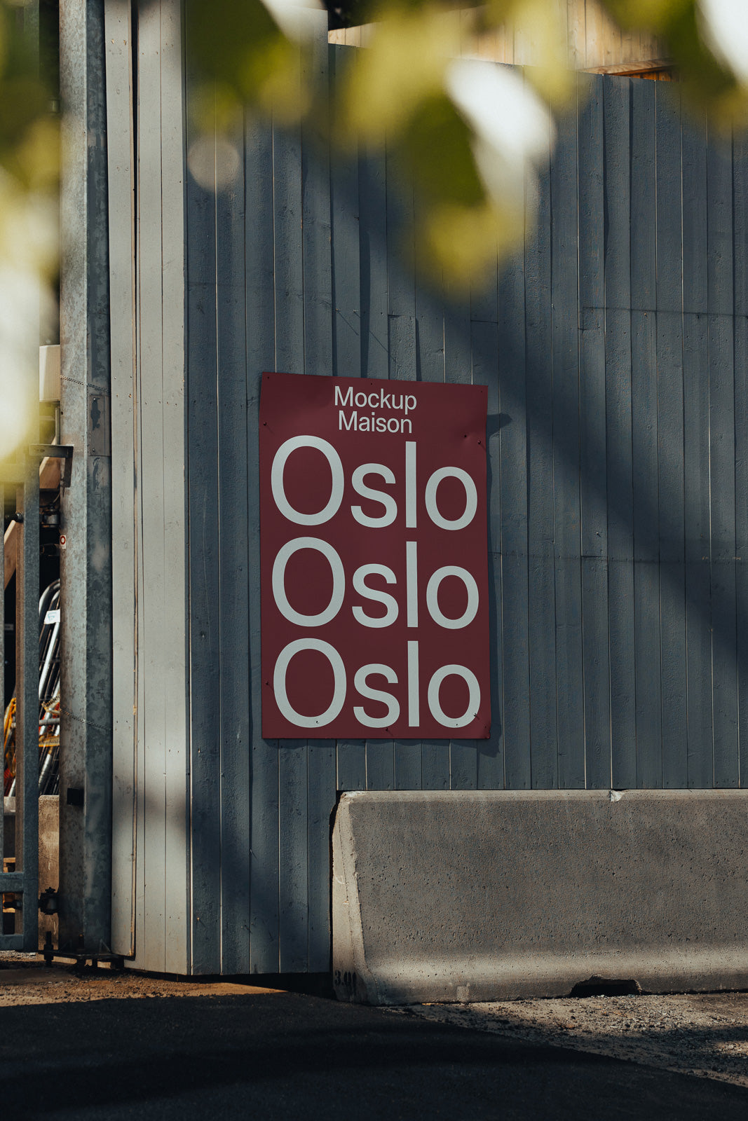 PSD mockup of a red poster with the text "Oslo" repeated three times, mounted on a wooden wall beside a concrete barrier.