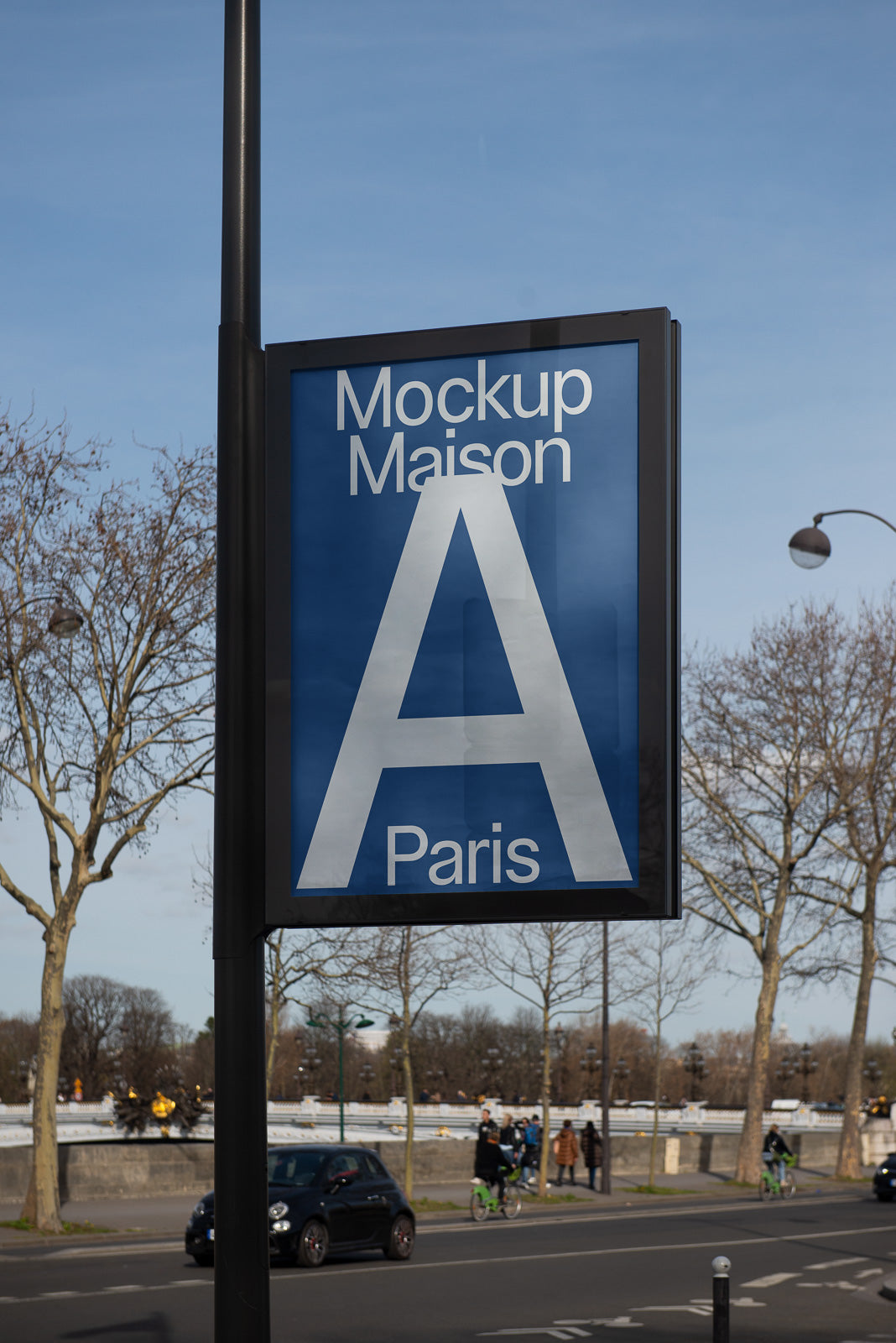PSD mockup of a street sign displaying bold text "Mockup Maison A Paris" in a clear urban setting with trees and road in the background.