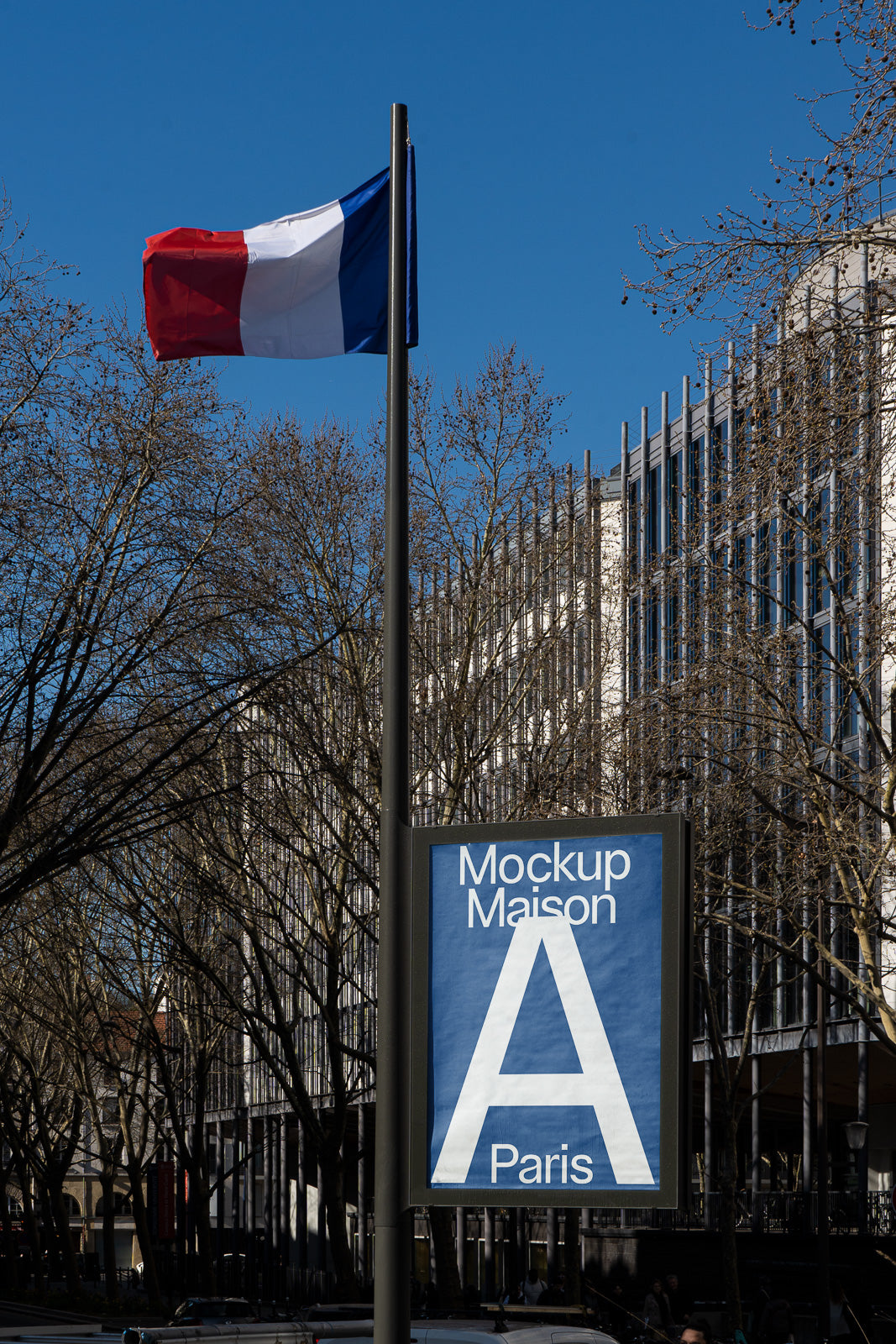 PSD mockup of a street sign displaying "Mockup Maison A Paris" in front of a French flag on a pole, with modern buildings and trees in the background.