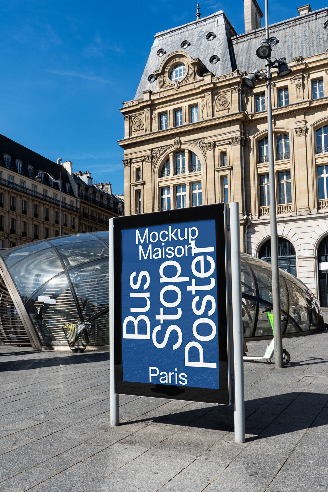 PSD mockup of a bus stop poster display in an urban setting with historic architecture in the background, blue sky, and modern glass structures.
