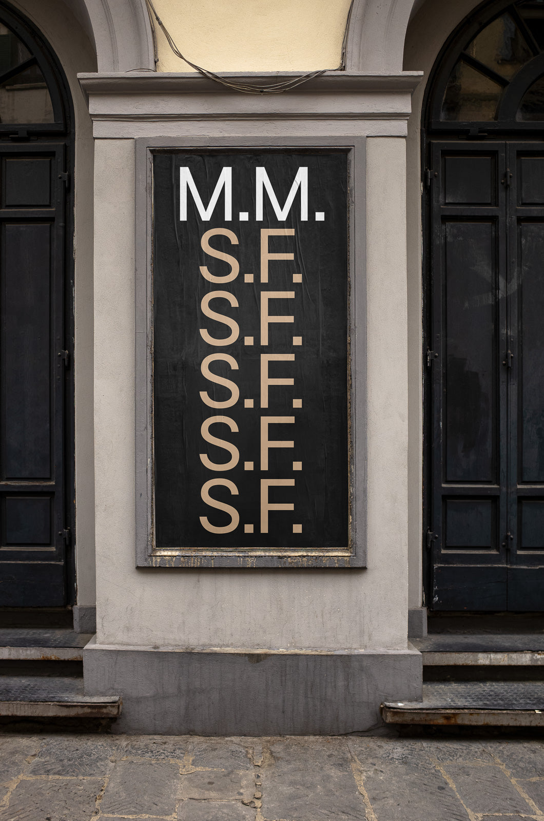 PSD mockup of a vintage-style poster on an exterior wall featuring large white and beige letters "M.M." and "S.F." on a black background, framed by gray stone.