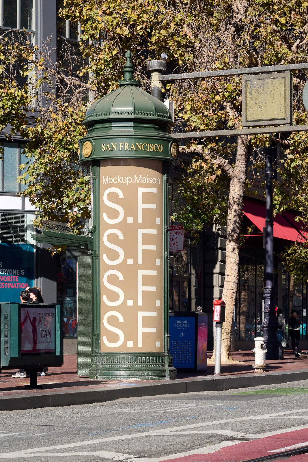 PSD mockup of a San Francisco kiosk with a large beige advertisement displaying repeated "S.F." text and surrounded by city buildings and trees.